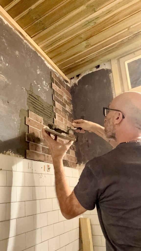 Posa di mattonelle sottili su un muro in ristrutturazione, malta e spatola